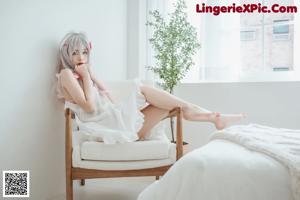 A woman in a white shirt and blue panties sitting on a bed.
