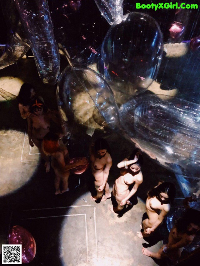 A group of naked people standing in a room filled with balloons.