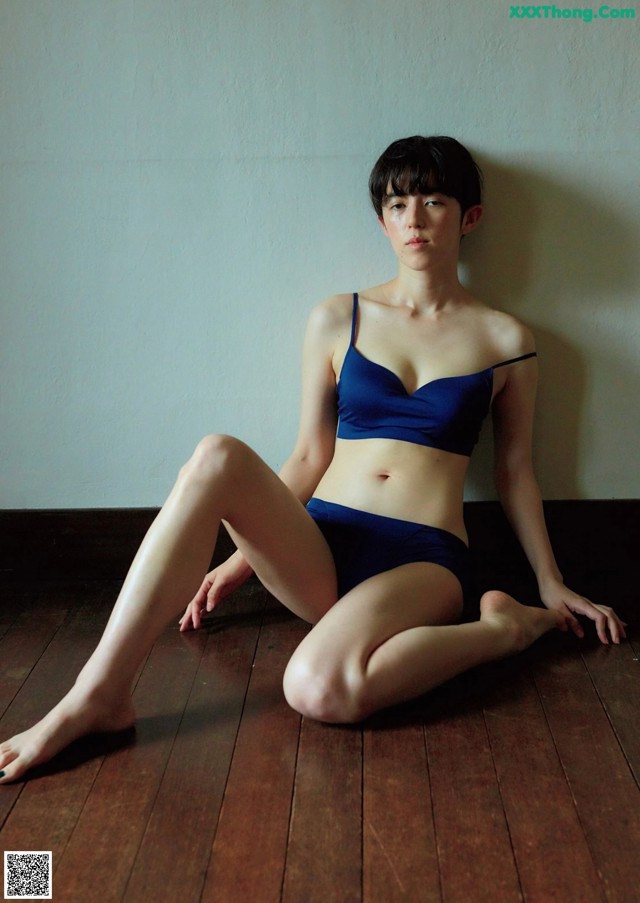 A woman in a blue bikini sitting on a wooden floor.