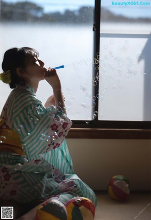 A naked asian woman sitting at a table with a bottle of water.