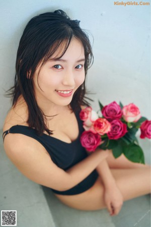 A woman in a black bathing suit holding a bunch of pink roses.