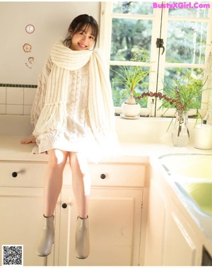 A woman in a white sweater leaning against a wall.