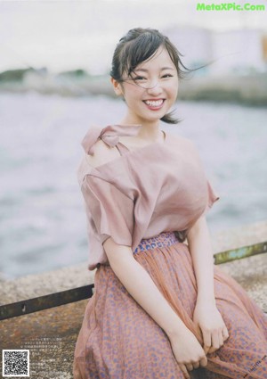 A woman in a pink dress leaning against a wall.