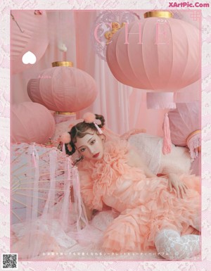 A girl in a pink dress sitting on a bed surrounded by pink lanterns.