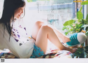 A woman in a blue sweater sitting on a bed.