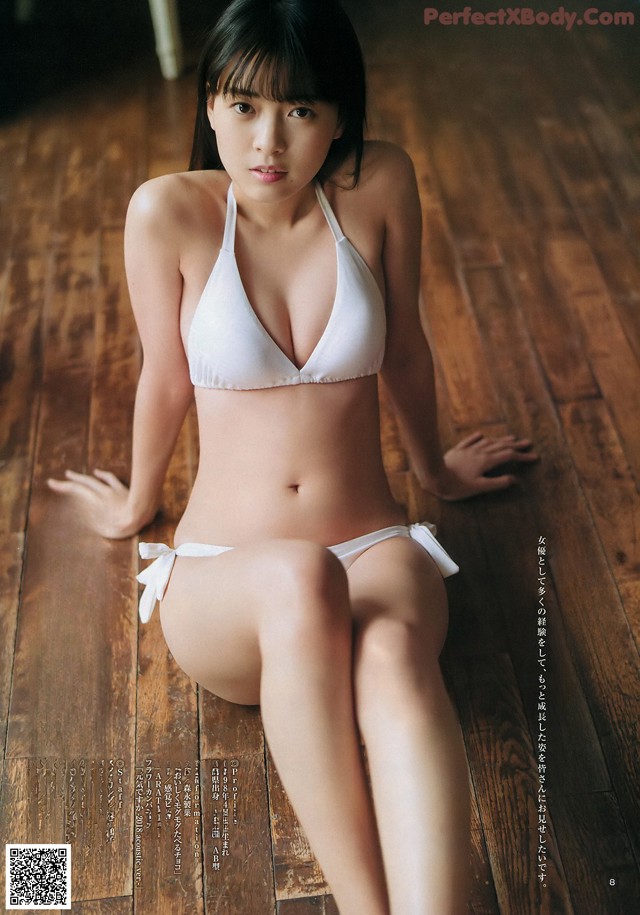 A woman in a white bikini sitting on a wooden floor.