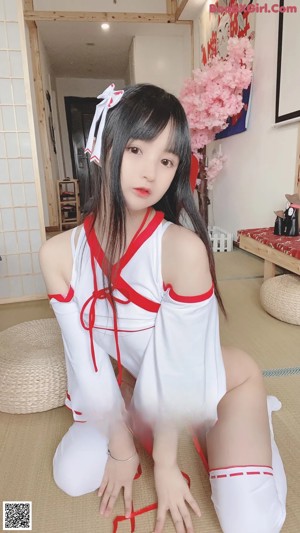 A woman in a white and red outfit is sitting on a bed.