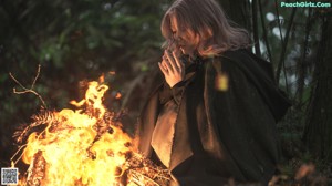 A woman sitting in front of a fire in the woods.