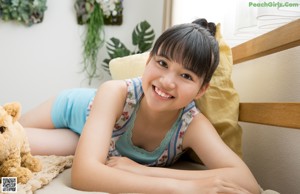 A young girl sitting on a bed with a teddy bear.