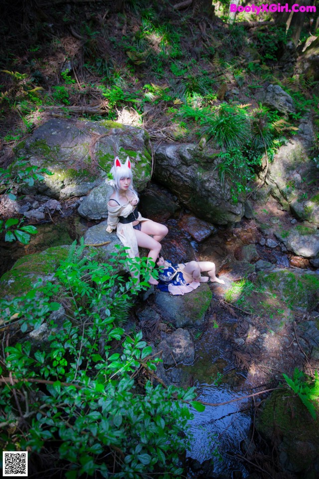 A woman sitting on a rock in the woods next to a stream.