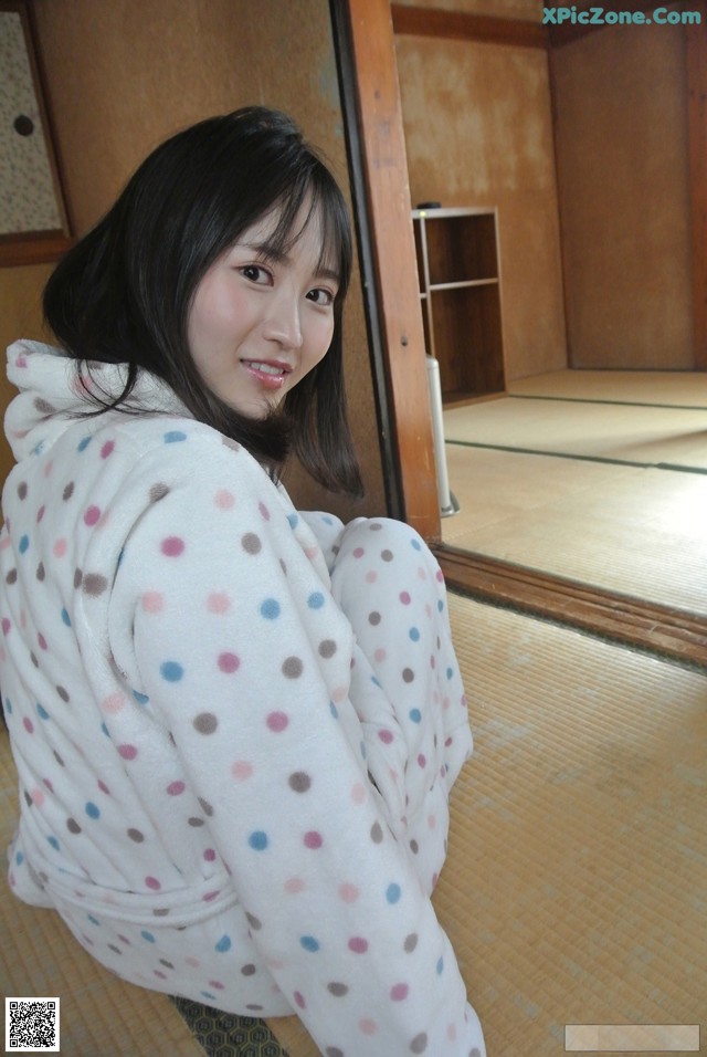 A woman in a polka dot robe sitting on the floor.