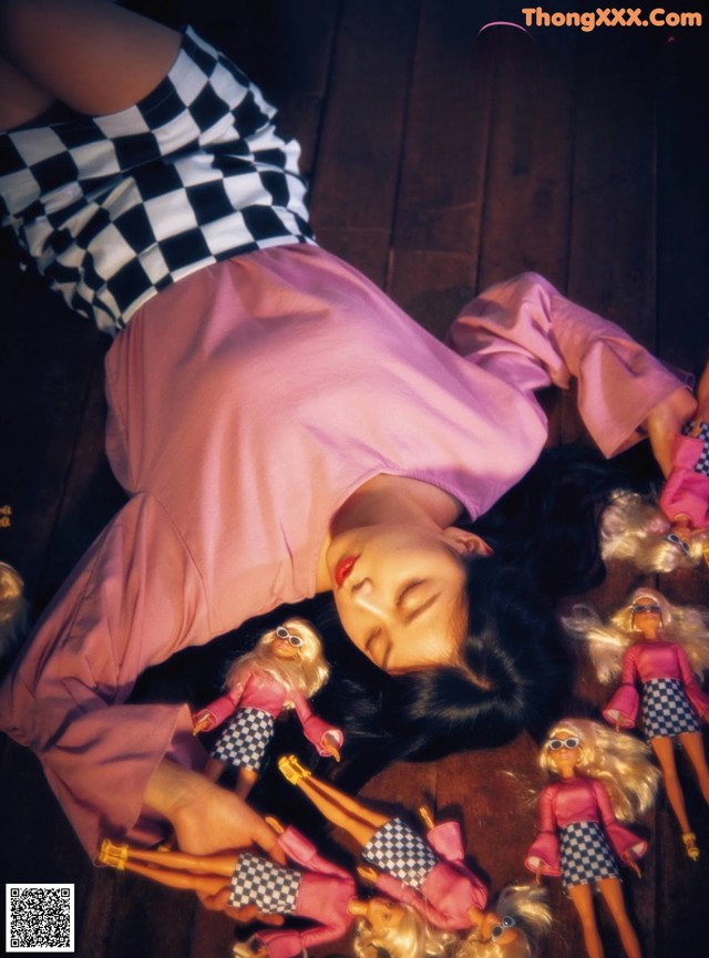 A woman laying on the floor surrounded by dolls.