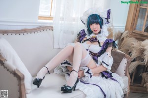 A woman in a maid outfit sitting on a bed.